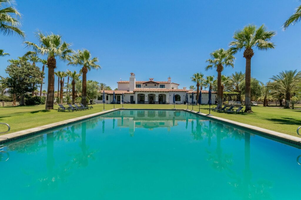 A large pool and house surrounded by palm trees at a Coachella event venue
