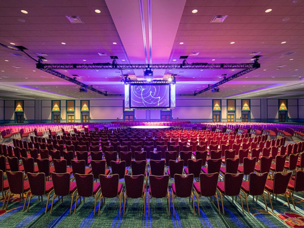 Loews Royal Pacific Resort at Universal Orlando with a central stage surrounded by red chairs and a large projection screen and rigged lighting from the cieling