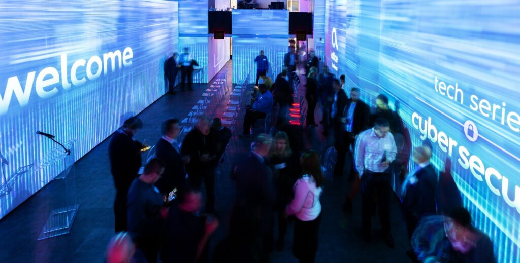 Projection walls with blue lights and graphics surrounding a networking event with people talking and mingling