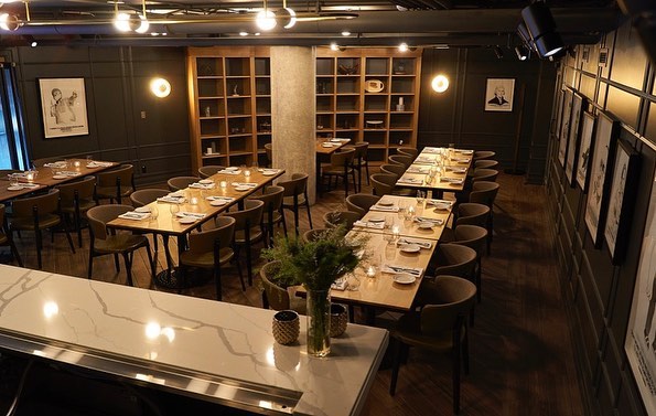 A dimly lit private dining room with four long tables and wall arts