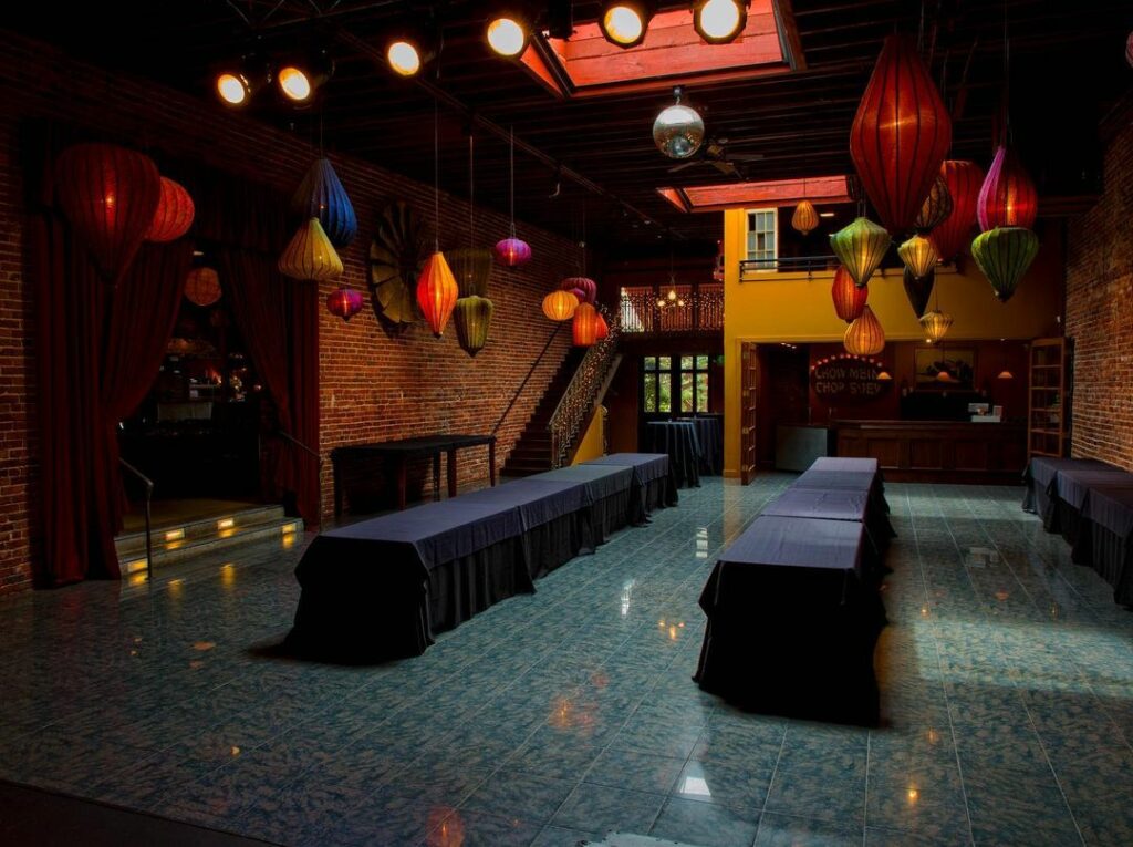 A brick wall room with colorful lanterns hanging from the ceiling, long tables covered in black cloths, adding to the overall sleek aesthetic of the space.