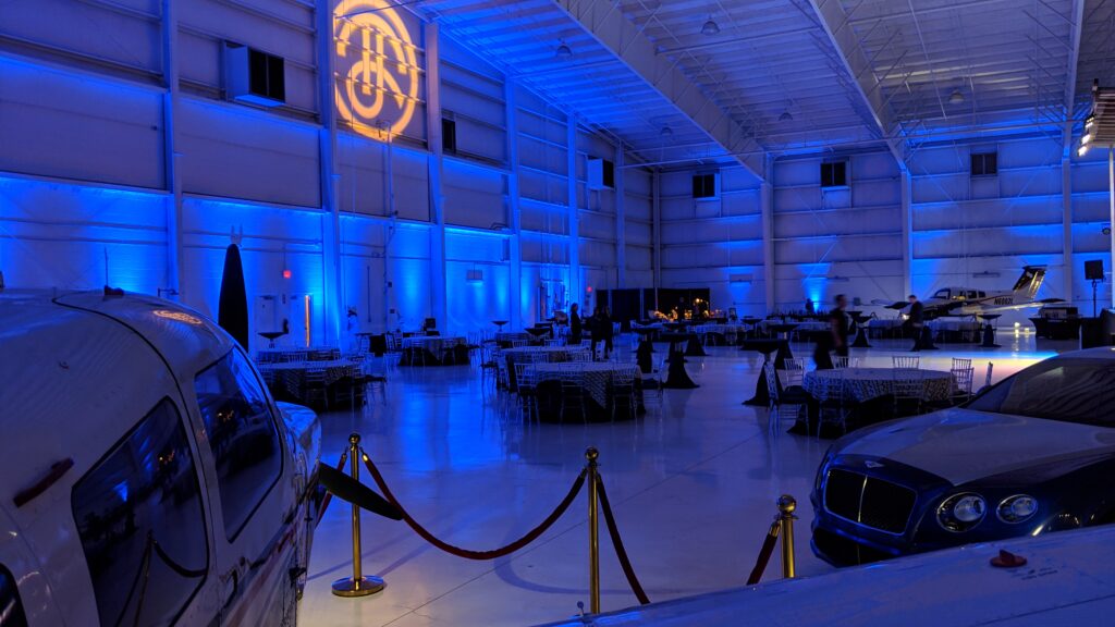 Industrial event space with high white ceiling, blue lighting and banquet table and chairs