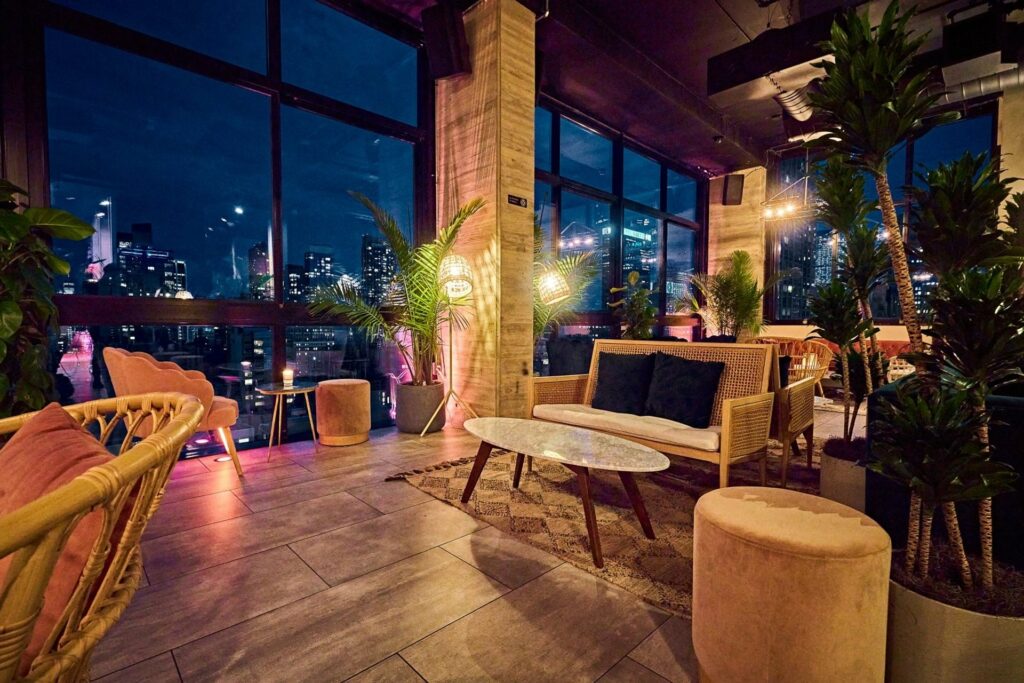 Rattan lounge furniture in a bar with large windows overlooking the city