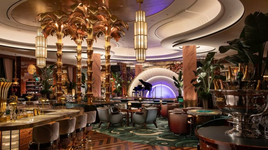 Opulent room with lounge furniture, gold palm tree statues, a bar and ovular ceiling details
