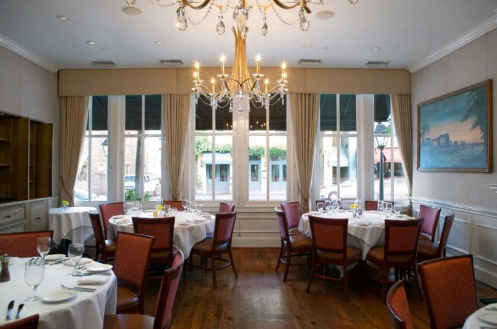 A private dining room featuring crystal chandeliers, upholstered walls, and large windows overlooking historic East Bay Street