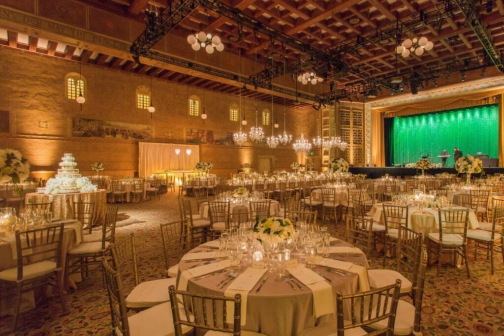 A huge ballroom with plenty of lighting, gold motif and a stage
