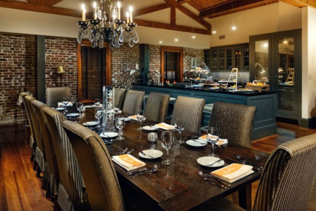 An elegant dining room with an open kitchen, exposed brick walls and a beuatiful chandelier