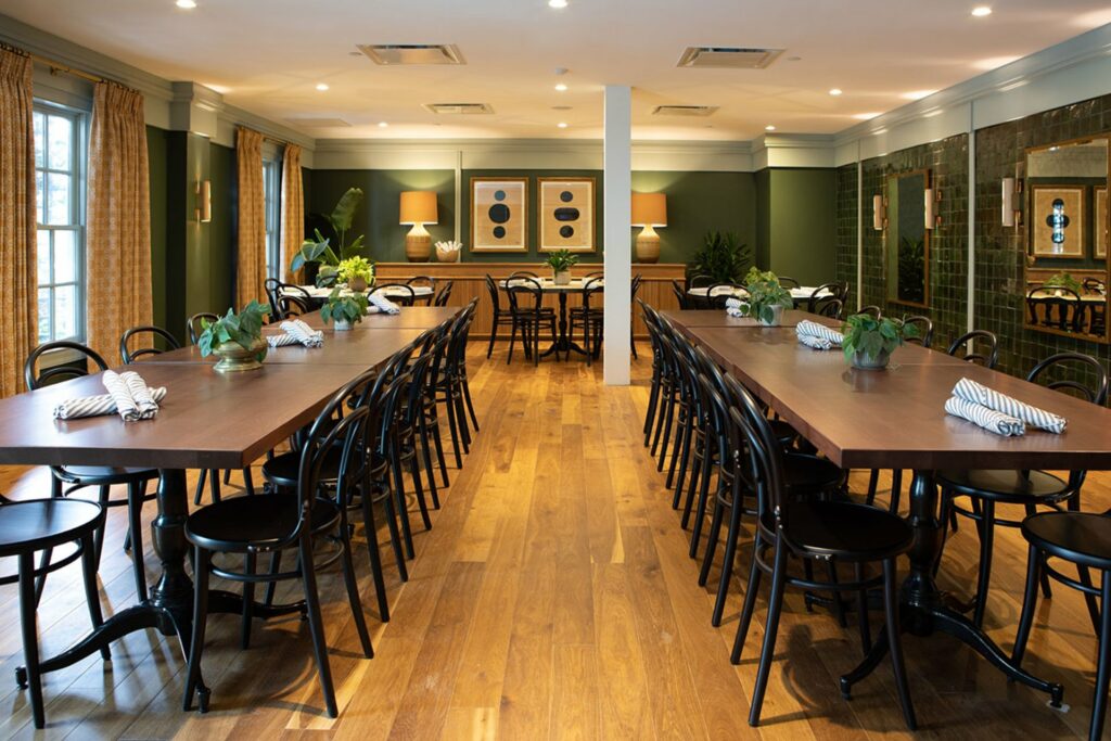 A cozy private dining room with 2 long tables on both sides, a round table  in the middle and big windows for natural lighting