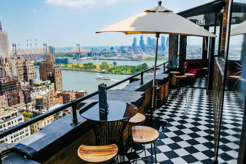 Rooftop bar with black and white tiled floor and patio seating and umbrella overlooking the city and river