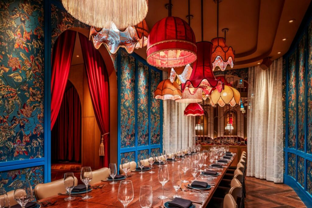 Ornate room with long table and red chandeliers, blue wallpaper and cream drapery