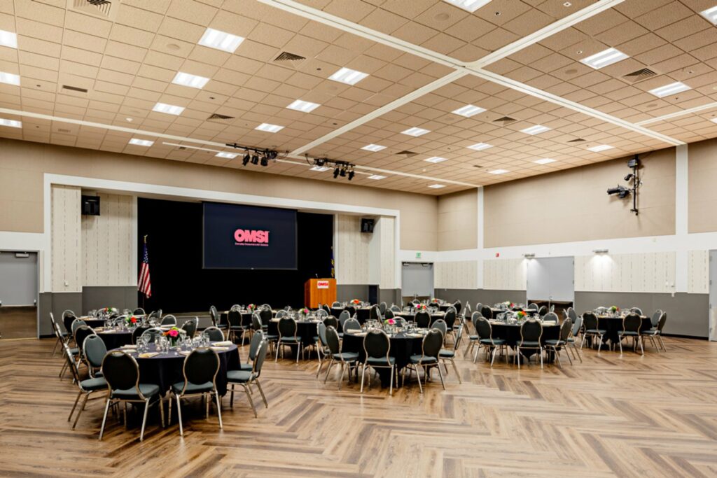 An event venue with audio and video equipments , a high ceiling, and  plenty banquet tables setup 