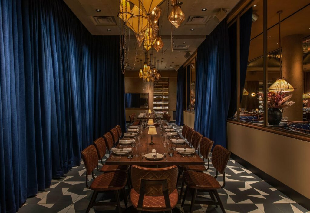 Private room with blue drapery and black and white floors with leather chairs and a long wooden table and chandelier overhead