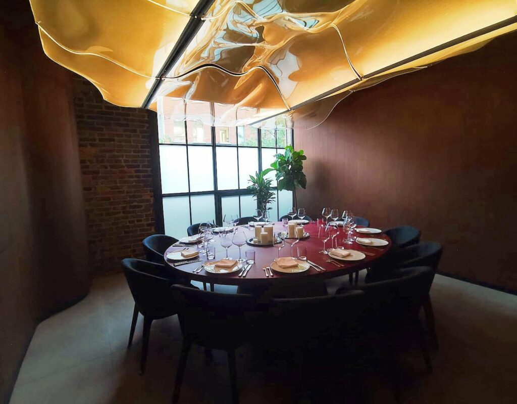 A private dining room with a unique light fixture, a floor to ceiling window for natural lighting and a huge round table in the middle 