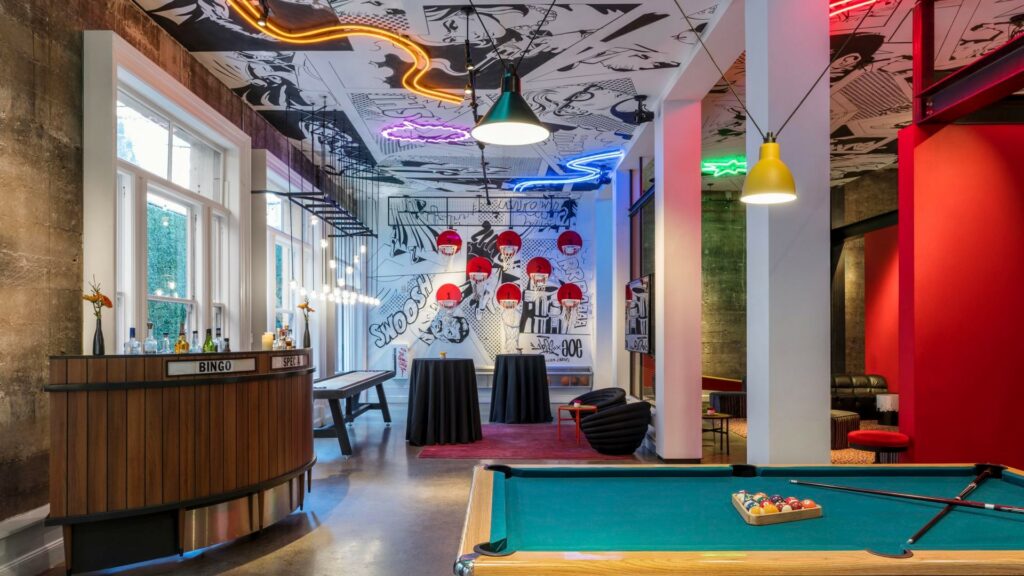 A modern-looking space with comic themed wall paint, plenty of lounge seats, a mini bar and a pool table