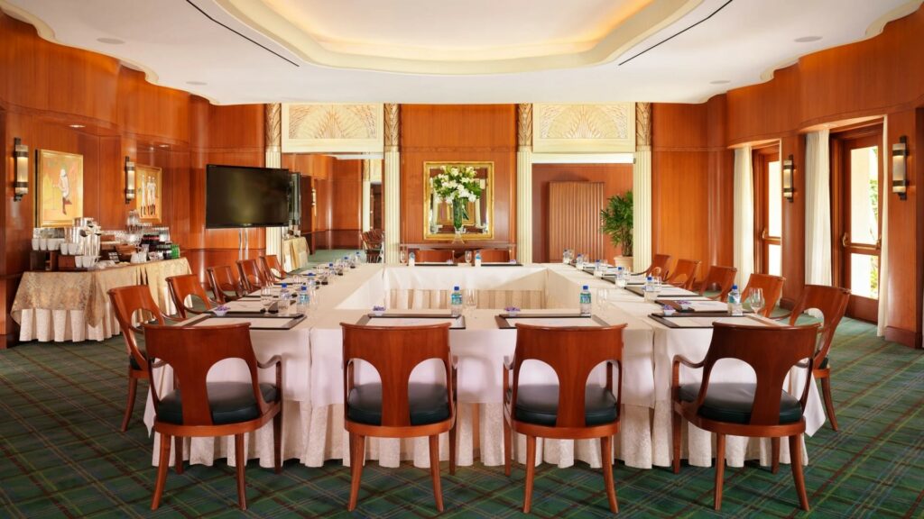An elegant conference room with a luxurious and traditional design, polished wooden panels line the wall, and table arranged in square and chairs around it. 