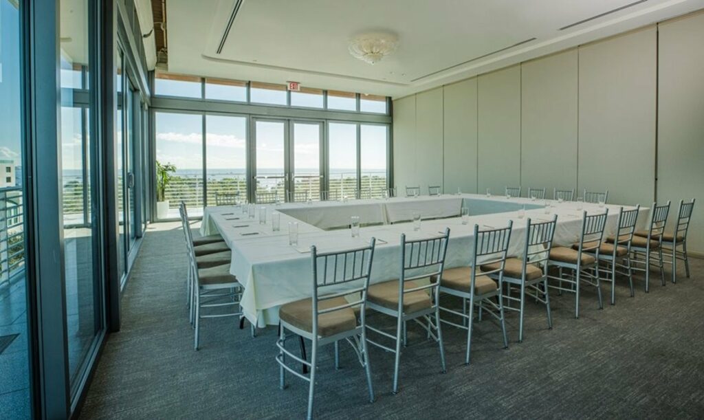 A meeting room with tables and chairs arranged in square and overlooking view from the outside through floor-to-ceiling windows. 