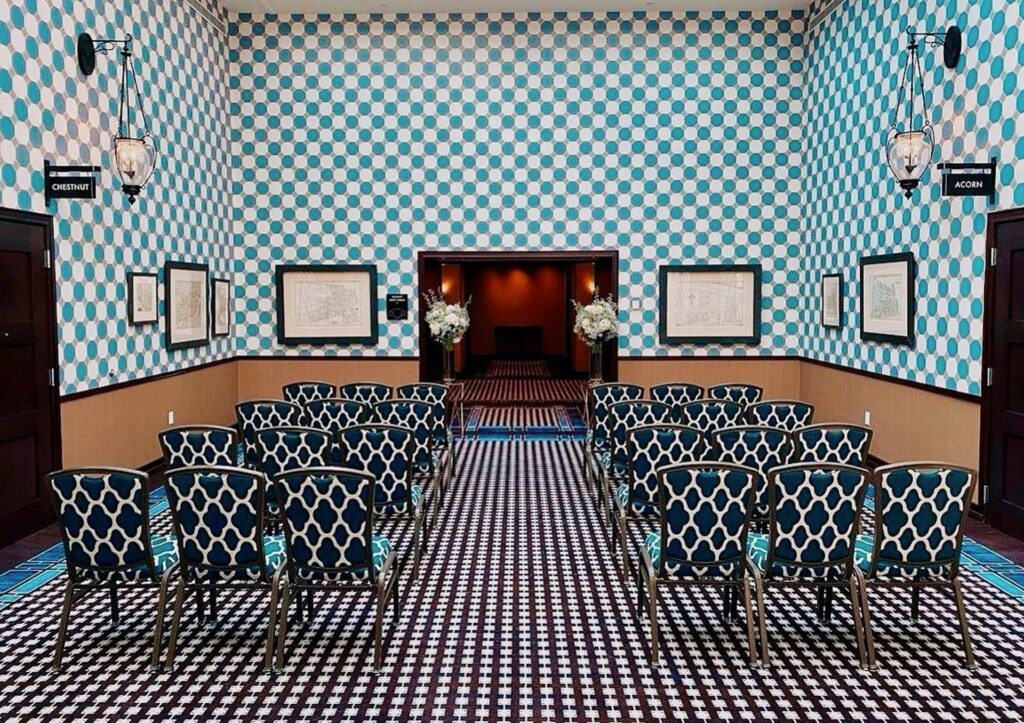 A room decorated with vibrant patterns from the wall, the chairs, and the flooring. The chairs are arranged in classroom style. 
