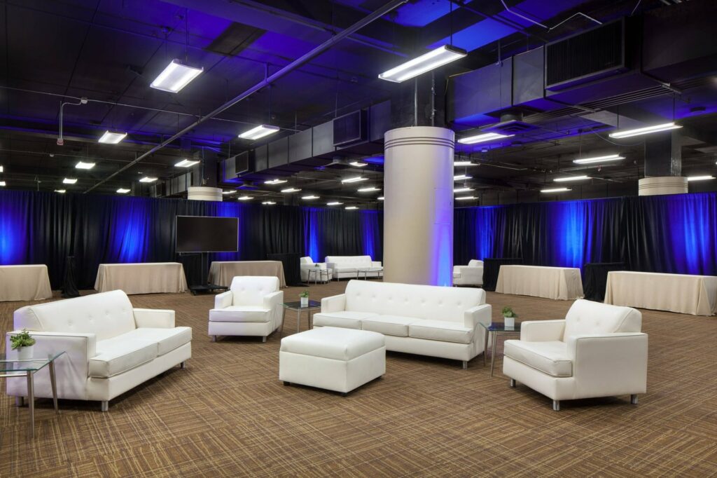 A huge room with high ceiling and white sofas at the center and long covered tables at the side. 
