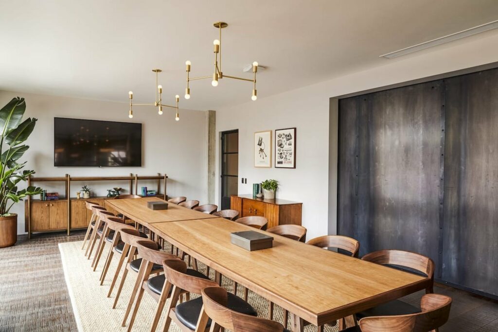 A meeting space with modern interior, a wooden long table in the middle and an LCD TV 