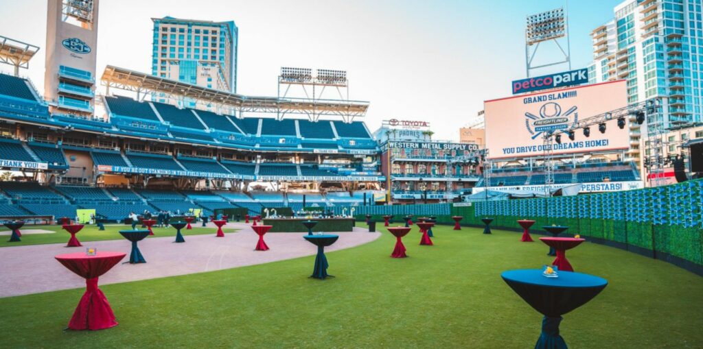 An outdoor stadium with high-top cocktail tables draped with red and blue linens scattered on the field. 