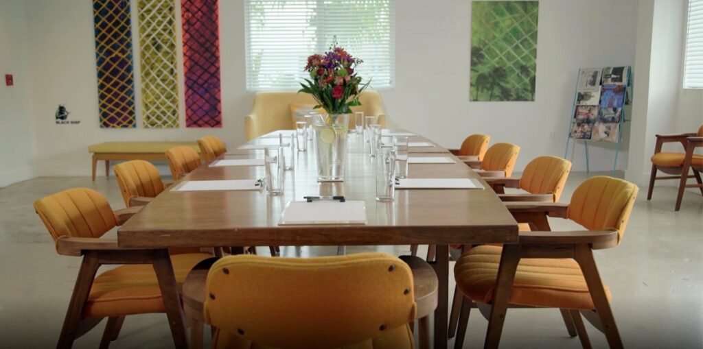 A cozy room with long wooden table, accompanied by comfortable mustard-colored chairs at the center. 