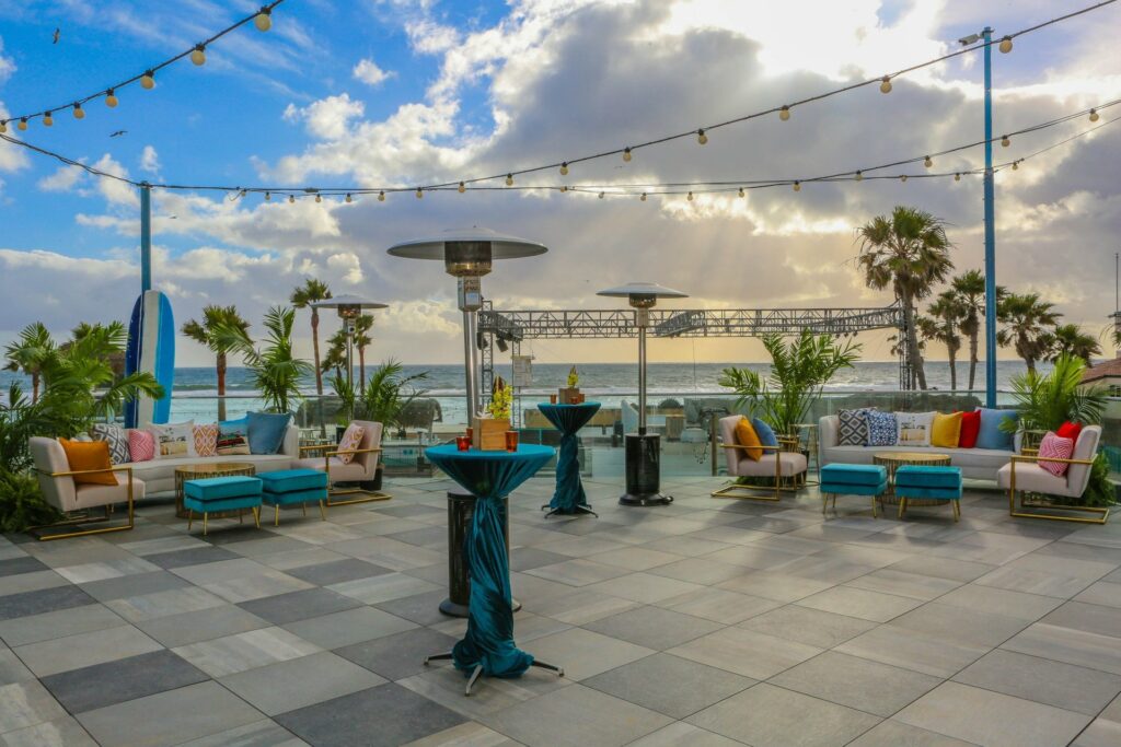 An outdoor space with overlooking view of the ocean, and colorful tables and chairs scattered throughout the space. 