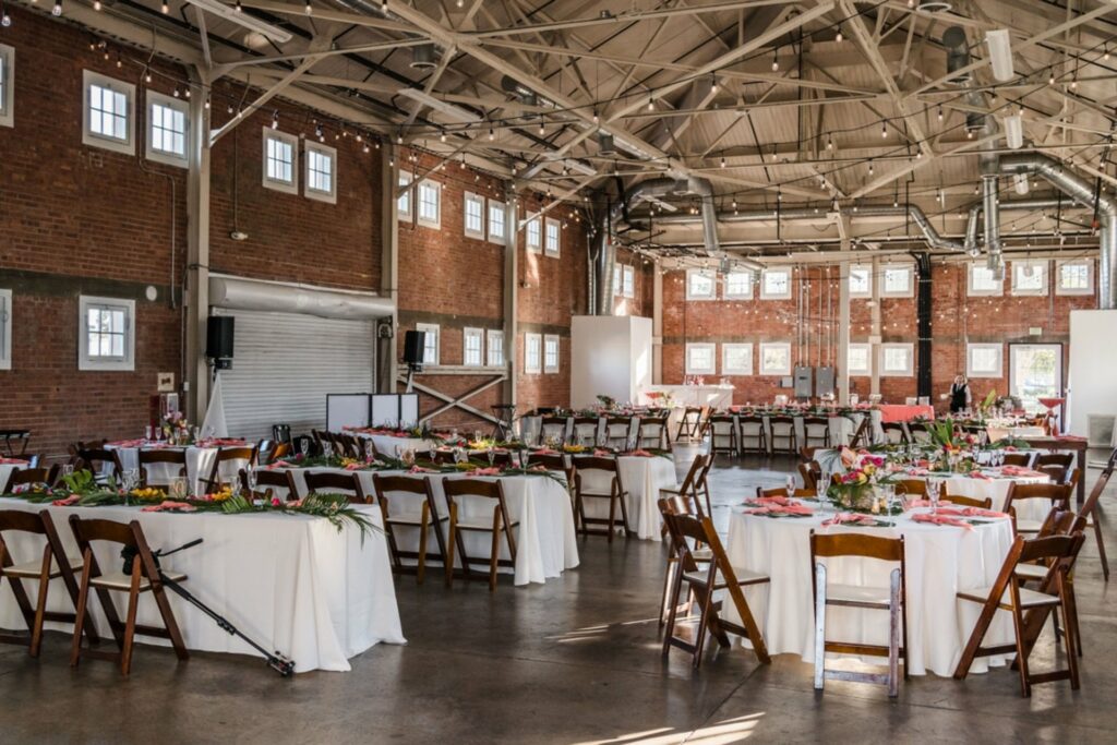 A spacious room with combination of red brick walls, ample natural light, expansive ceilings, and tables and chairs arranged elegantly. 