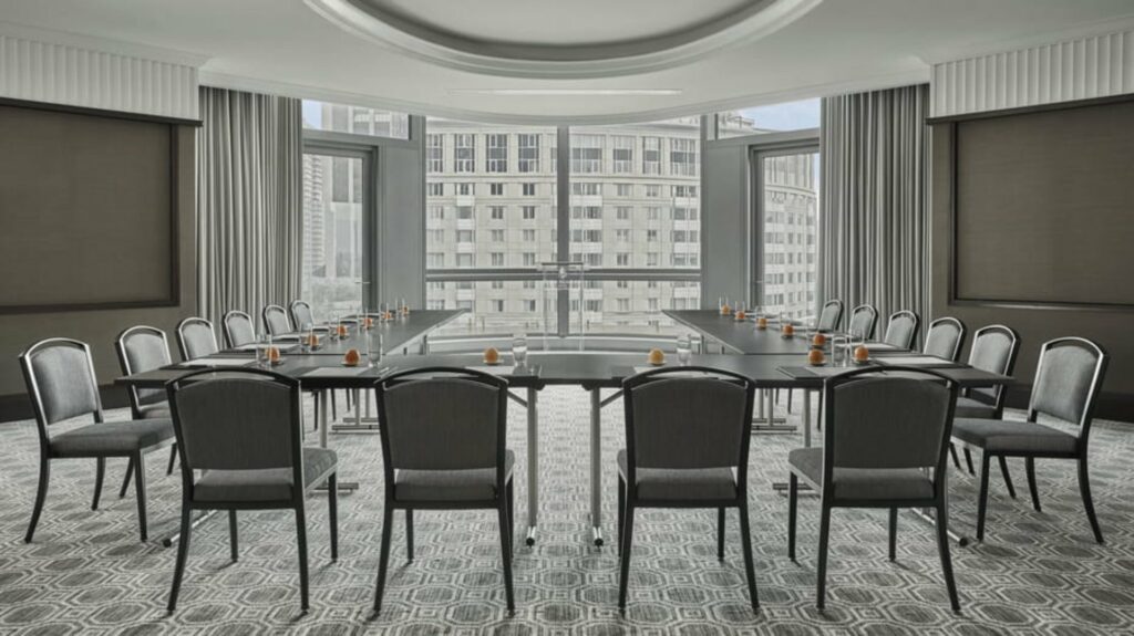 An elegant meeting room with overlooking view from the outside from the floor-to-ceiling windows, with tables and chairs arranged in U-shaped. 